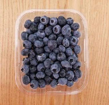 Plastic punnet full of lush blueberries against wood grain background Stock Photos