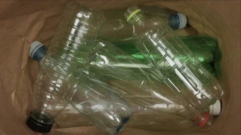 Plastic recycle bottles get thrown into a brown bag, close-up Stock Footage