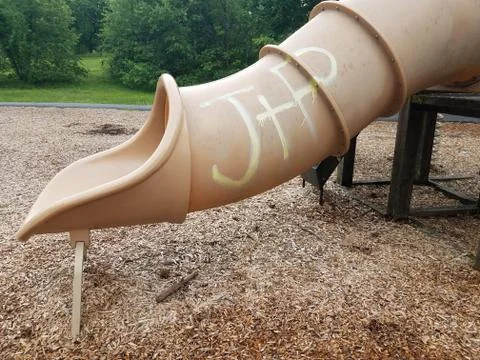 Plastic slide on play structure with graffiti and wood chips Stock Photos