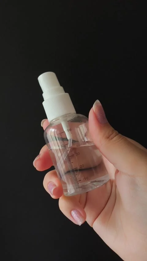 A plastic spray bottle with a milliliter mark in a womans hand on a black 動画素材 314975305