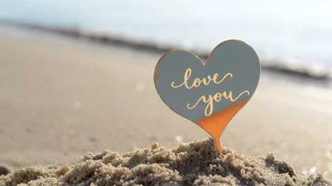 Plastic stick shape of heart with words Love you sand beach sea shore background Stock Footage 257545370