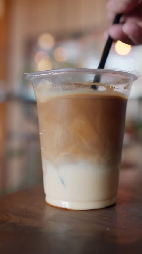 Plastic straw being inserted into an iced latte in a clear plastic cup Stock Footage 346279962