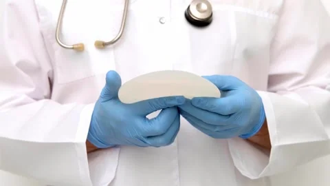 Plastic surgeon blue gloves squeezing  breast implant  demonstrate elasticity, a Stock Footage 342615554