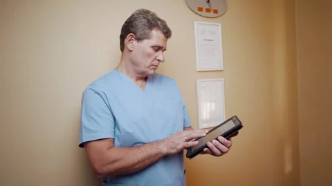 A plastic surgeon in uniform uses a digital tablet in his office. Stock Footage 256157194