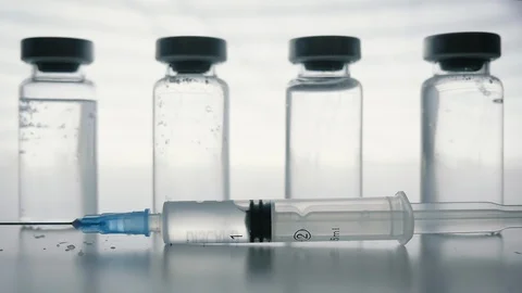Plastic Syringe Falling in Slow Motion in Front of Glass Vaccine Bottles Stock Footage 106254450
