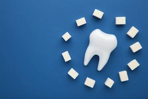 Plastic tooth with sugar on dark blue background. Caries and sugar concept. D Stock Photos