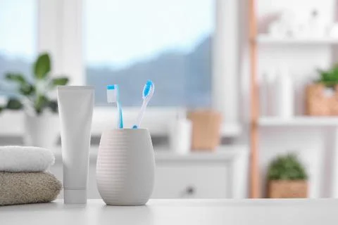 Plastic toothbrushes in holder, toothpaste and towels on white table indoor.. Stock Photos