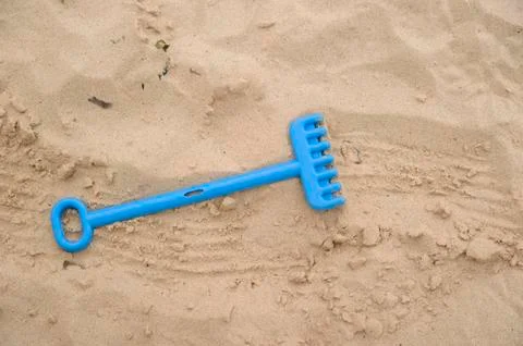 Plastic toy rake on sandy beach Stock Photos