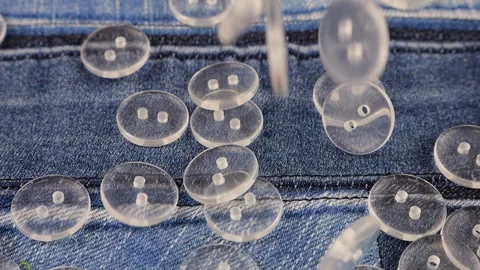 Plastic transparent buttons fall on denim. Slow motion. Video stock 229486348