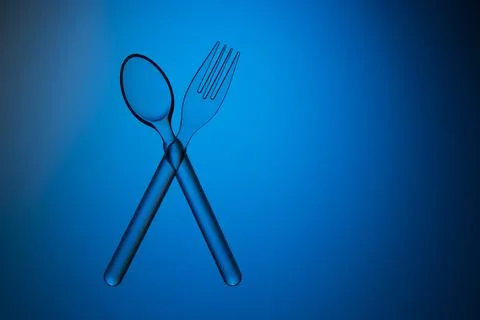 Plastic transparent spoon and fork crossed on a blue background. Stock Photos