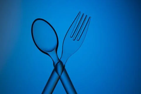 Plastic transparent spoon and fork crossed on a blue background. Stock Photos