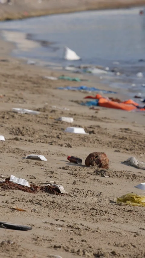 Plastic trash and household waste scattered on a sandy beach by the waterline. E Stock Footage 345879555