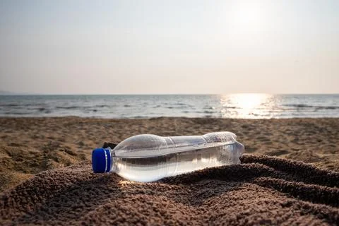 Plastic water bottle lying on beach towel beside the sea at sunset. Hydrati.. Stock Photos