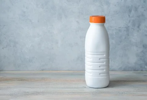 A plastic white bottle without a label with an orange cap on a gray background. Stock Photos