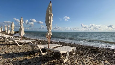 Plastic white deckchairs with a closed umbrella on an empty beach. Video stock 117102910