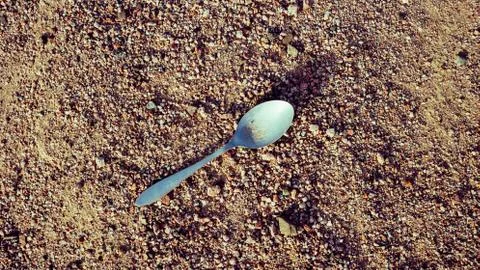 Plastic white spoon lying on beach Stock Photos