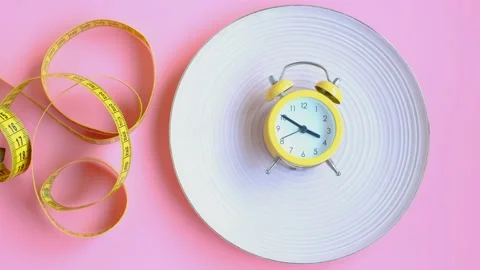 Plate with alarm clock and centimeter tape on pink background, intermittent Stock Footage 230389540