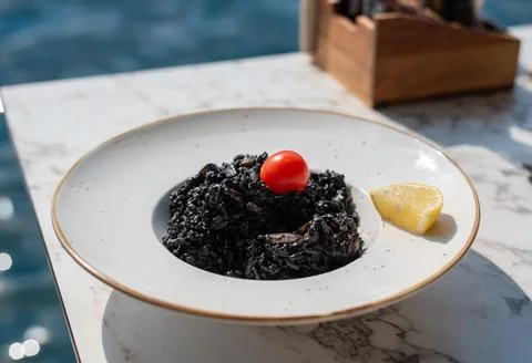 Plate of black squid ink risotto with a cherry tomato and lemon Fotos Stock