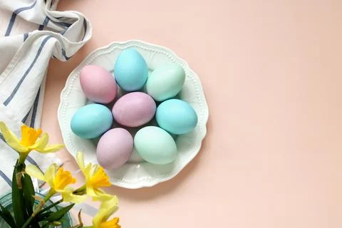 A plate with colored Easter eggs and a bouquet of daffodils on a pink backg.. Stock Photos