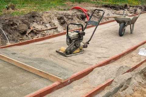 Plate compactor levels sand base for brick sidewalk inside curb frame, read.. Stock Photos