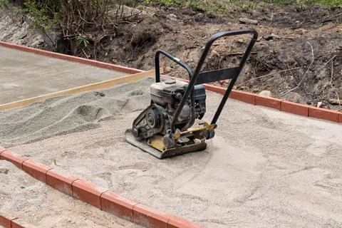 Plate compactor rests on sand base inside curb as paving walkway is prepared Stock Photos
