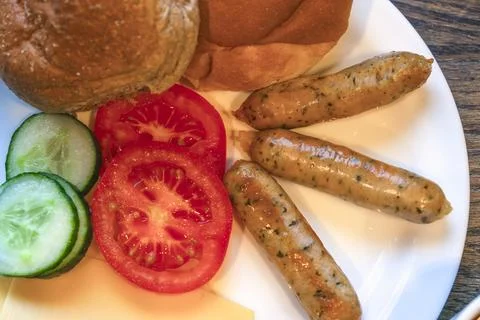 Plate with cooked sausages bread rolls sliced tomatoes and cucumbers top view Stock Photos