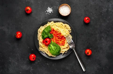Plate of cooked spaghetti with tomatoes and basil on black Stock Photos