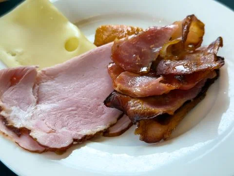 A plate with crispy bacon, sliced ham, and Swiss cheese, creating a Stock Photos