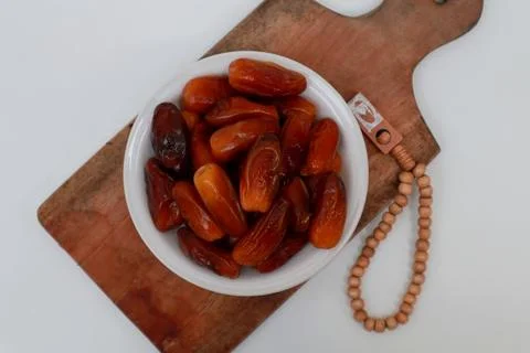 A plate of dates and prayer beads on a wooden cutting board Stock Photos