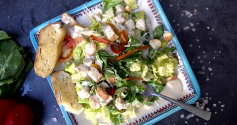 Plate of delicious salad surrounded by vegetables and salt on black surface Stock Footage 168633585