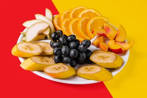Plate with different fruits on yellow and red background Stock Photos