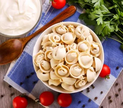 Plate of dumplings on the kitchen table with sour cream and vegetables. Top v Stock Photos