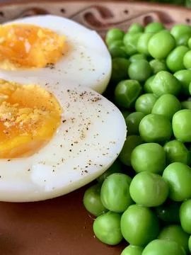 A plate features soft-boiled eggs cut in half alongside vibrant green peas, Stock Photos