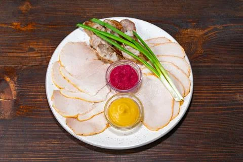 A plate features thinly sliced cold cuts accompanied by two sauces Stock Photos