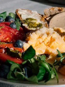 Plate featuring scrambled eggs alongside fresh tomatoes, juicy blueberries Stock Photos