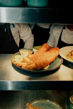 A plate of fish and chips is on a counter in front of a group of people Stock Photos