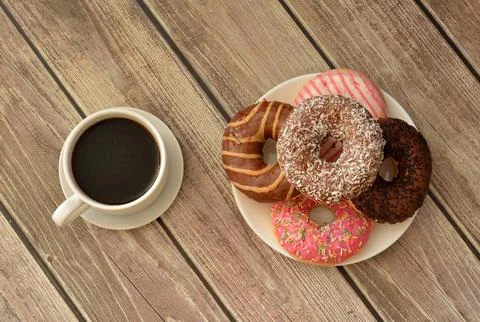 A plate with five donuts in multi-colored glaze and a cup of hot black coff.. Stock Photos