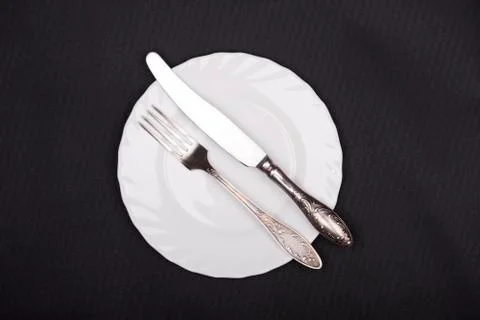 Plate, fork and knife top view on black cloth background Stock Photos