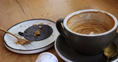 Plate with fork near half empty coffee cup and bill on wooden countertop Stock Footage 314345101