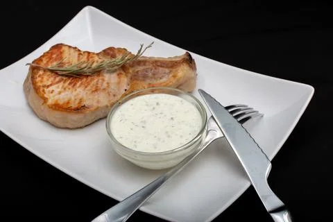 On the plate is a fork, a serving knife, white sauce and pork steak Stock Photos