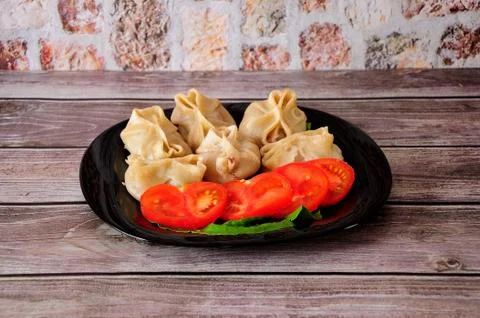 Plate with freshly cooked manti on a lettuce sheet and sliced tomato on a woo Stock Photos