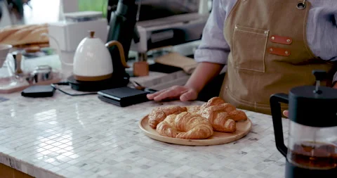 Plate full of croissants being held by asian senior woman in apron behind coffee Stock Footage 320523950