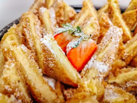 A plate of golden, crispy triangular pastry slices dusted with powdered sugar 库存照片