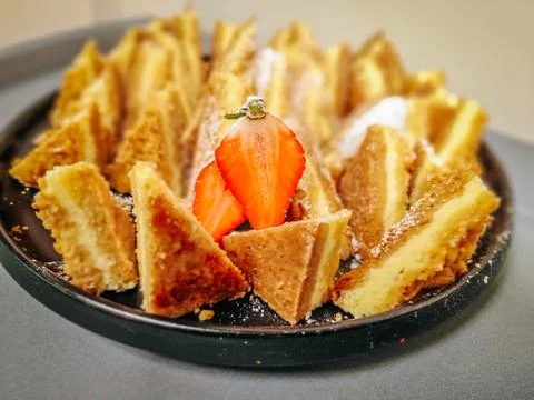 A plate of golden, crispy triangular pastry slices dusted with powdered sugar 库存照片