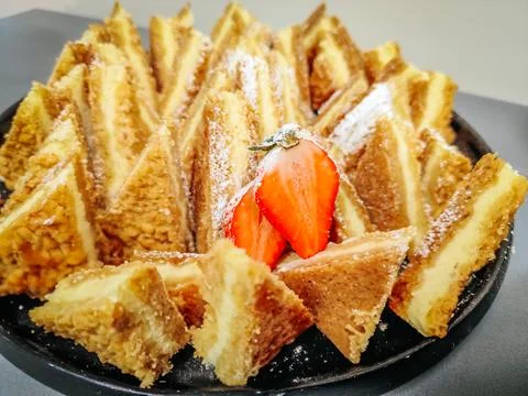 A plate of golden, crispy triangular pastry slices dusted with powdered sugar 库存照片