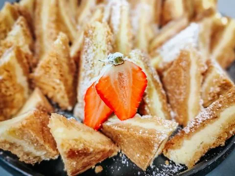 A plate of golden, crispy triangular pastry slices dusted with powdered sugar Stock Photos