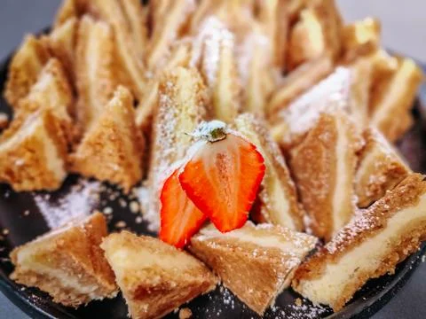 A plate of golden, crispy triangular pastry slices dusted with powdered sugar 库存照片