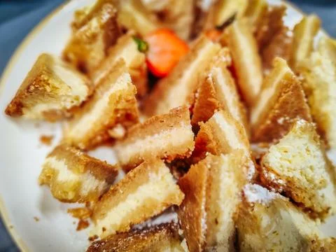 A plate of golden, crispy triangular pastry slices dusted with powdered sugar Stock Photos