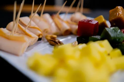 Plate of ham rolls, fruit paste, cheese cubes, and nuts with blurry background Stock Photos
