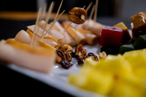 Plate of ham rolls, fruit paste, cheese cubes, and nuts with blurry background Stock Photos